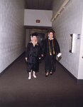 Two students walking through hallway wearing commencement regalia